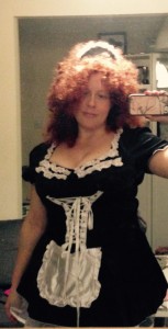 Photograph taken in the mirror of me wearing a French maid outfit, red frizzy permed wig and smiling