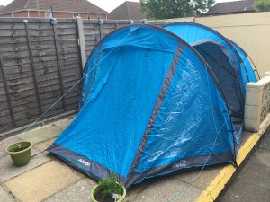 Image shows front quarter angle of erect tent with flower pots holding it in place with the side door open