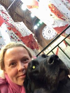 Selfie of me with Guide Dog Fizz with the Climbing Centre behind us and showing a large round stain glass window at the top Centre of the photograph