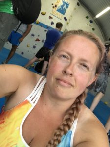 Selfie photograph of me sat inside VauxWall with people climbing behind me and the signage for VauxWall behind me