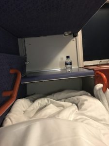 Photograph is taken from where I sat in the bottom bunk in the berth, showing the width of the bed, with a counter at the end of the bed and the sink with a bottle of water on the side