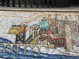 Photograph of Mosaic at Glasgow Queen Street railway station, showing the river cliyde and bridge on the left and the buildings of Glasgow on the left.