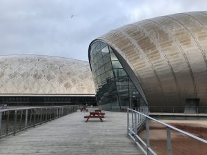 Photograph is taken of the rear of the IMAX building where Starbucks sits amongst a glass wall sat beside part of an old dock area