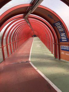 Photograph of red steel girders of a covered over path and cycle path, showing the red and green paths with an arch over the top which is totally enclosed 