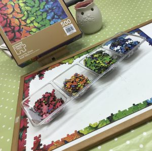 Image of a white board with all the edges of the colourful jigsaw pieces on it.  Sat in the centre is a tray with the separated colours in.