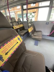 Side on view of grey seats on a bus with many have yellow tape explaining about social distancing on the aisle seats and on both seats every other row