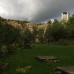 Image of the high quarry walls of Ratho EICA garden, with dark storm clouds behind creating a bright reflection of light from the sun from behind the photographers