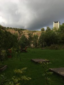 Image of the high quarry walls of Ratho EICA garden, with dark storm clouds behind creating a bright reflection of light from the sun from behind the photographers