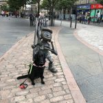 Fizz sat in front of a Mini the Minx statue on the street in Dundee