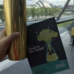 Photograph of my gold Starbucks travel mug with the guide book to The Glasgow Science Centre with the SEC Armadillo building behind across the river Clyde.