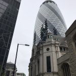 Photograph of The Gherkin building behind a church with the side of The Cheesegraer on the very left of the photo