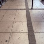 Flooring in a bus station, showin dirty cream large paving slabs with smaller rectangular darker tiles at key points, like where the notice boards are, where the benches are and what area is free from furniture in the middle.