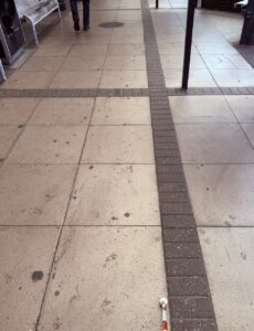 Flooring in a bus station, showin dirty cream large paving slabs with smaller rectangular darker tiles at key points, like where the notice boards are, where the benches are and what area is free from furniture in the middle.